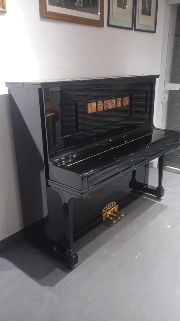 Shiny black upright piano with three gold pedals in a room with framed pictures above it.