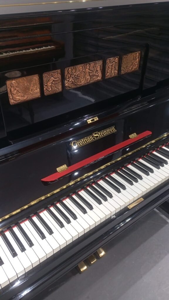 Black Grotrian-Steinweg upright piano with decorative copper-toned tiles on the music panel and white/black keys visible below.