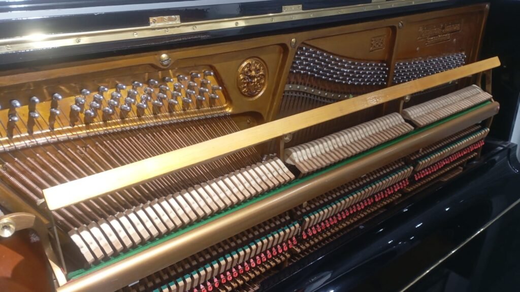 Inside of a piano showing its string harp, hammers, and action mechanism with wooden rails and metal pins