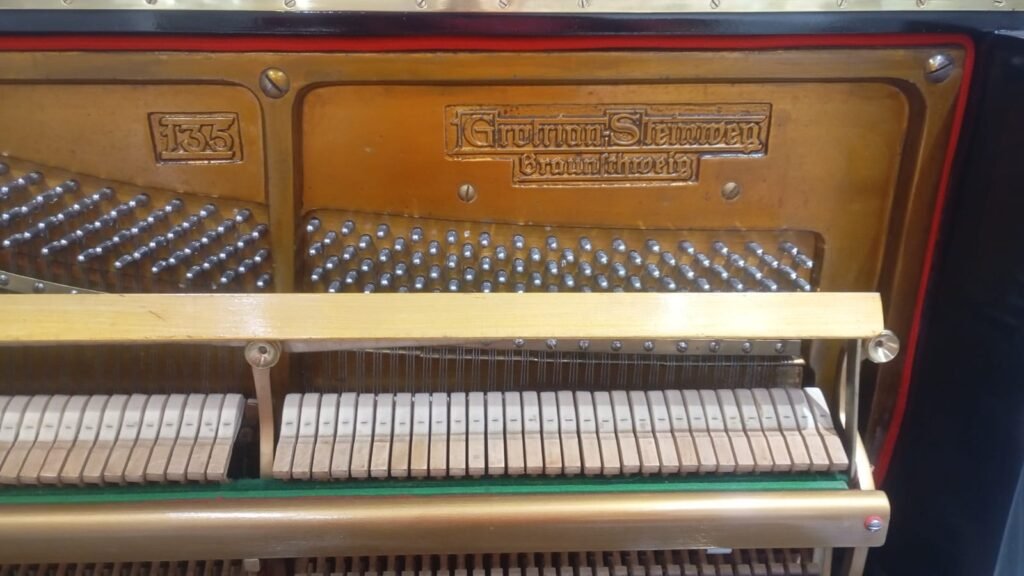 Close-up of the inside of a vintage upright piano, showing hammers, tuning pins, and a brass plate with the number 135.