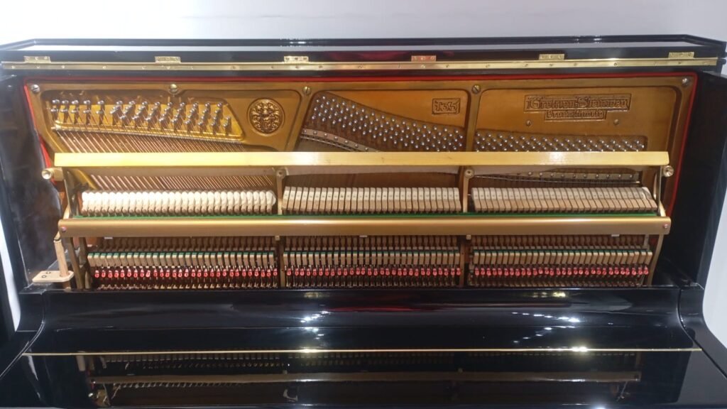 Open upright piano showing its internal action: hammers, strings, and dampers visible inside a polished black cabinet